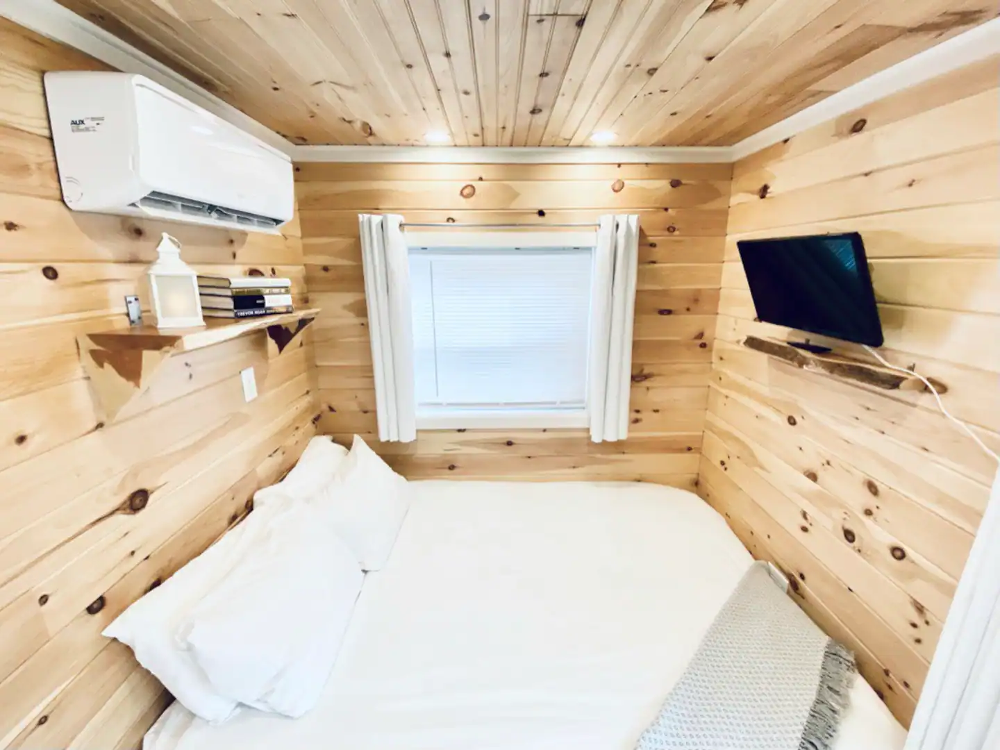 A comfortable resting room with cotton bedding and live edge shelves, a SmartTV, a selection of books, and a bespoke candle for ambiance